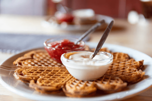 Waffle on a plate with jam and sour cream